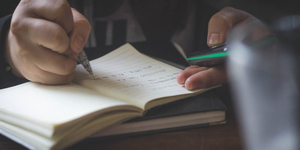 Image of a person taking notes and checking their phone